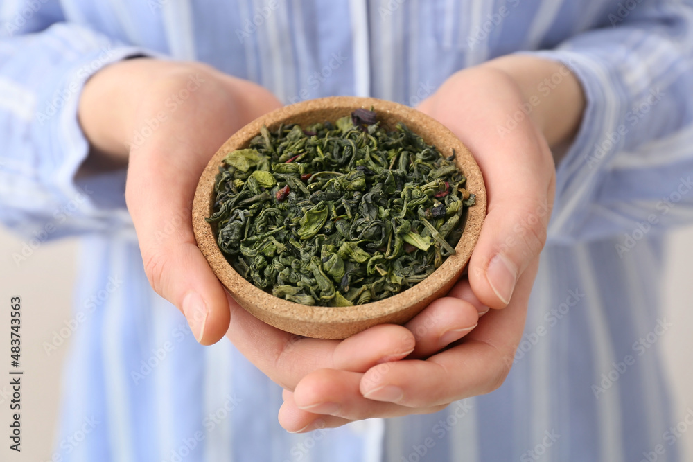 Woman holding plate with dried green tea leaves, closeup