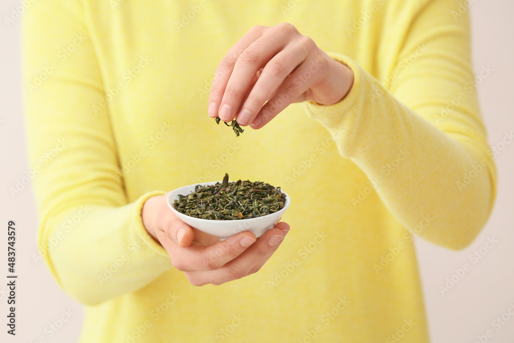 Woman holding plate with dried green tea leaves on light background, closeup