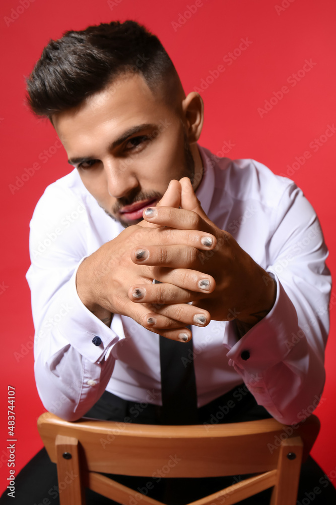 Portrait of businessman with stylish manicure sitting on chair on color background