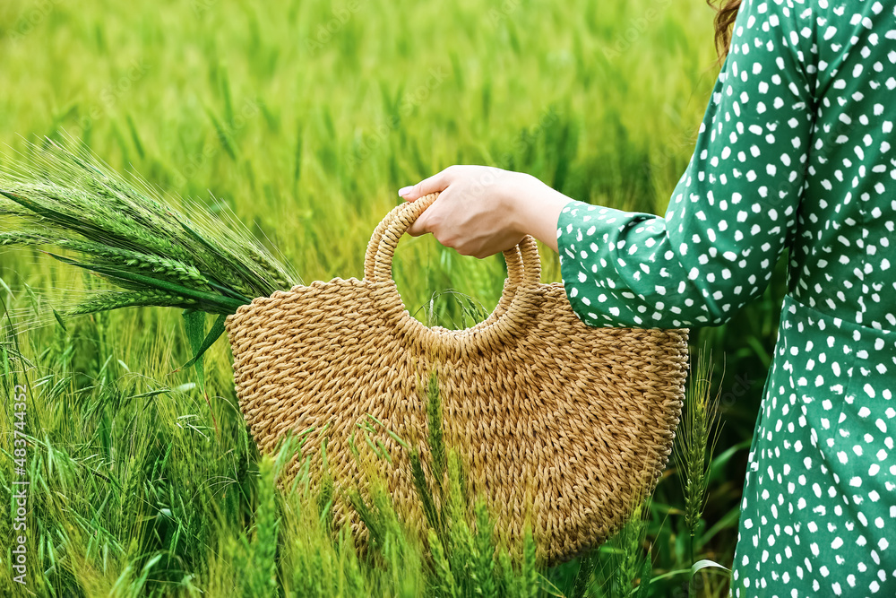 Woman with wicker bag and wheat spikelets in field