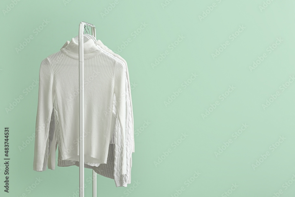 Rack with clean white sweaters on green background