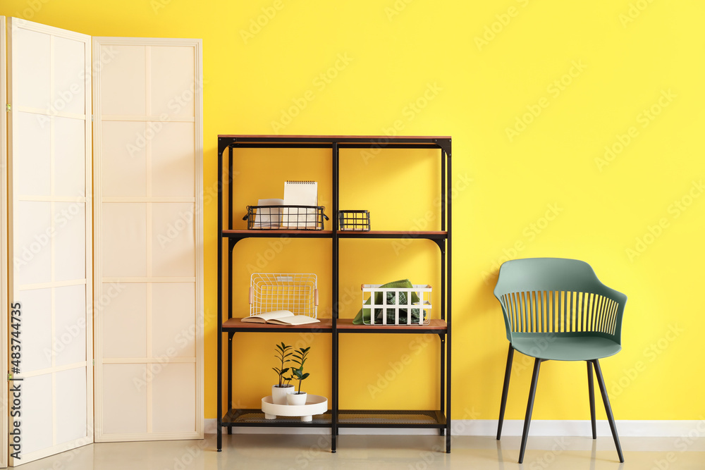 Shelf unit with decor and chair near color wall