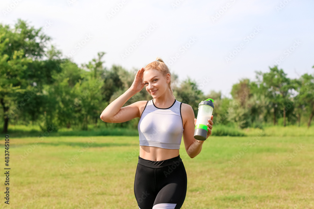 Young woman in sportswear holding bottle of protein shake outdoors on sunny day