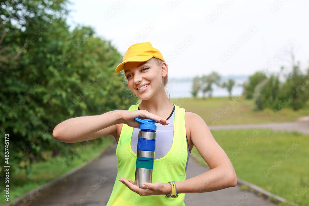 Young smiling woman in sportswear holding bottle with protein shake outdoors