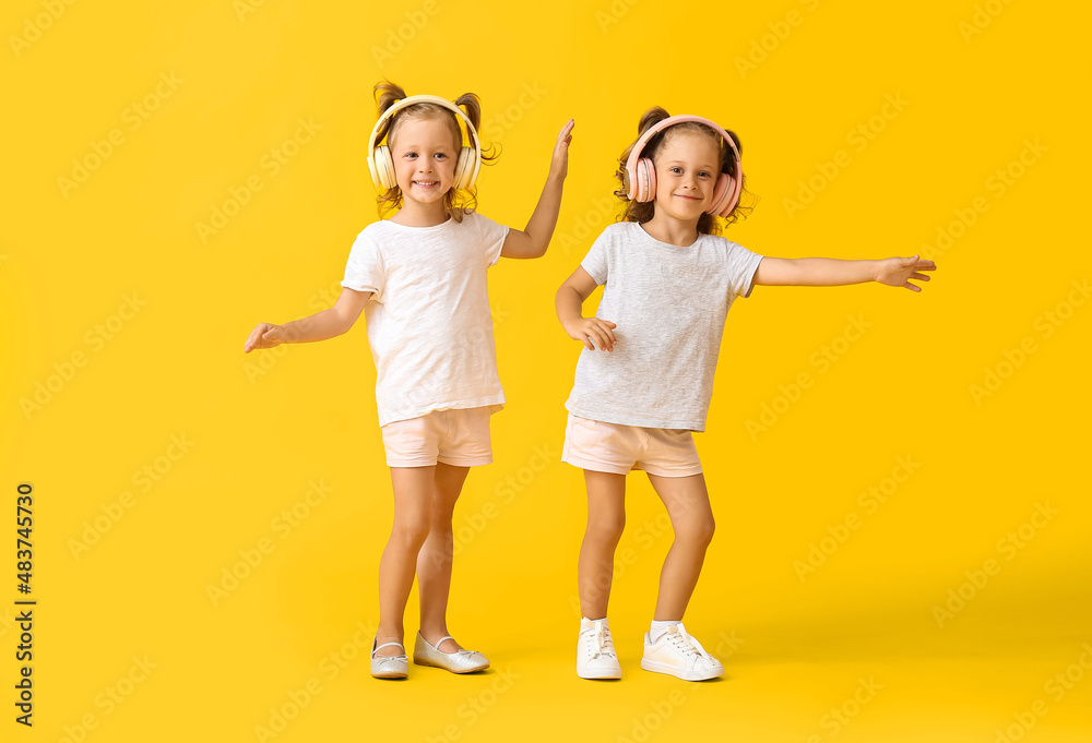 Cute little girls in headphones dancing on yellow background