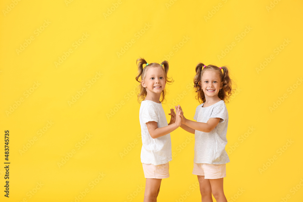 Cute little girls with ponytails holding hands on yellow background