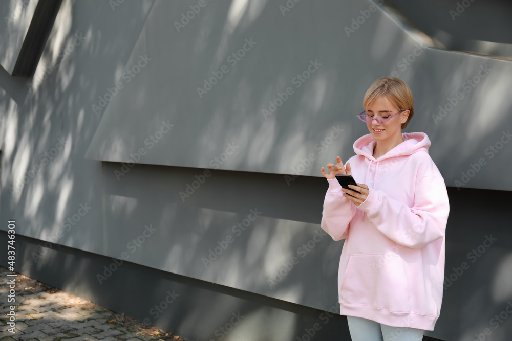 Beautiful young woman in stylish hoodie and with phone outdoors