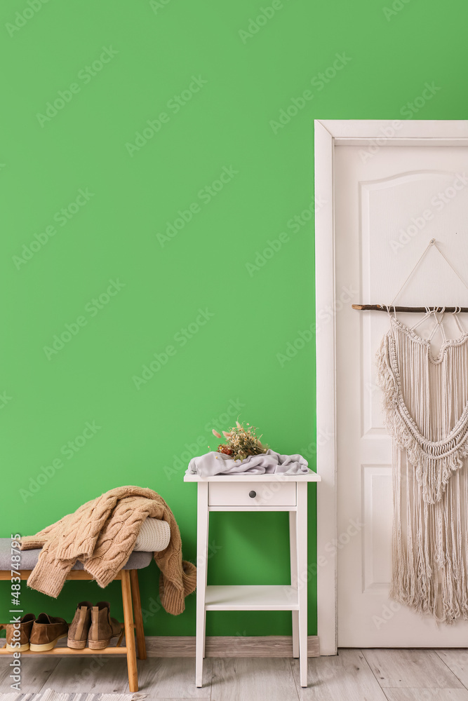 Stylish table and pouf with sweater near green wall in hallway