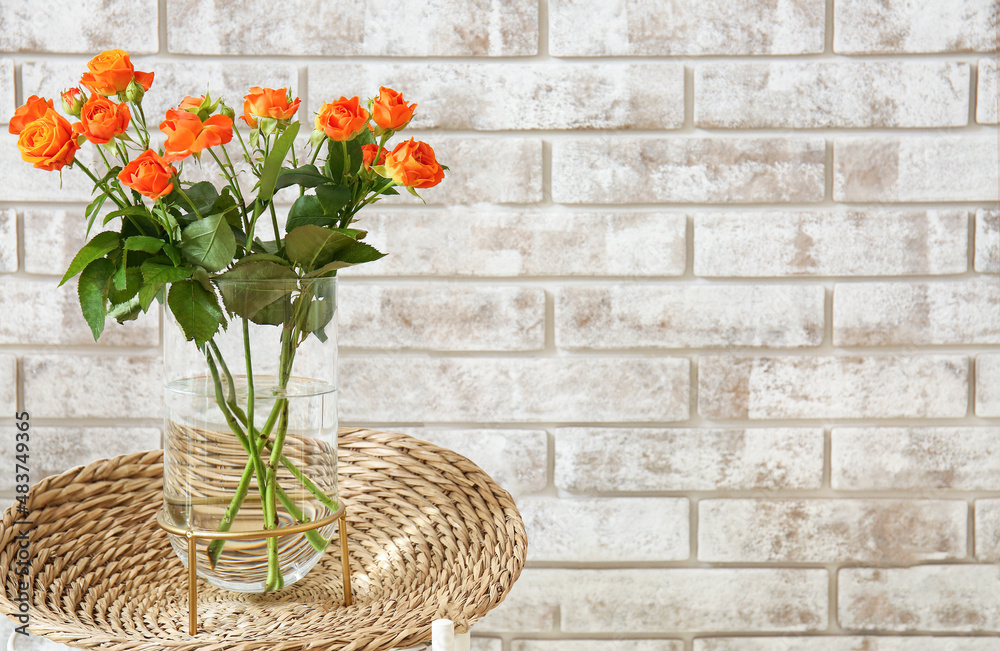 Vase with beautiful orange roses on table against brick wall