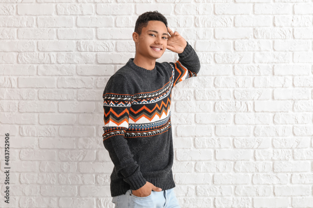 Handsome African-American guy in knitted sweater on white brick background