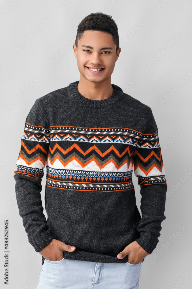 Handsome African-American guy in knitted sweater on light background