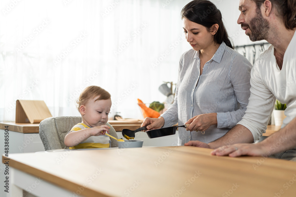 Caucasian beautiful parents take care of baby boy toddler in kitchen. 