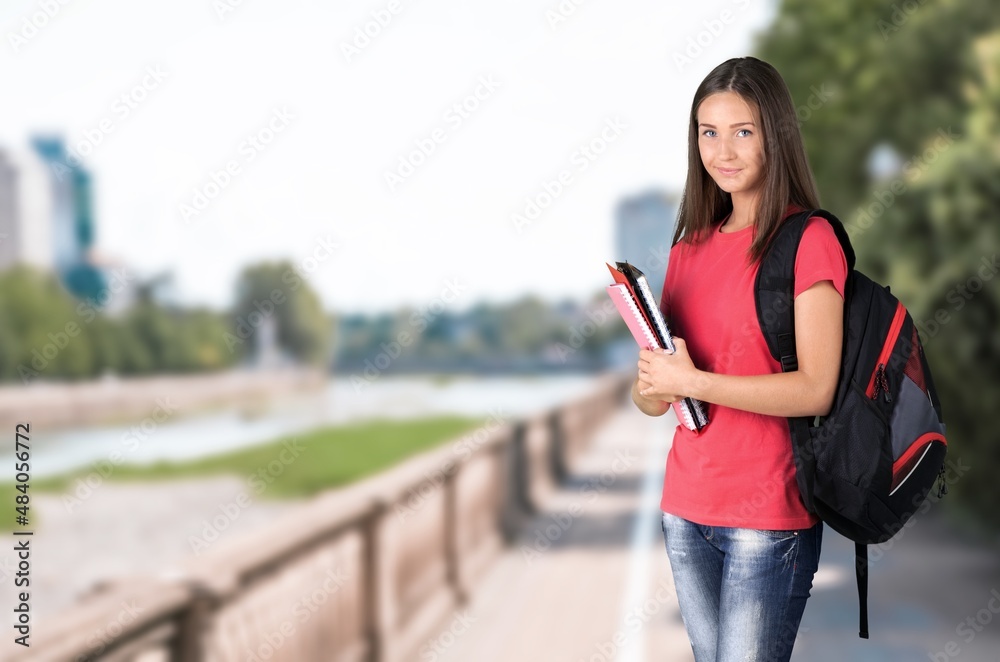 Female student standing outdoors university holding books.