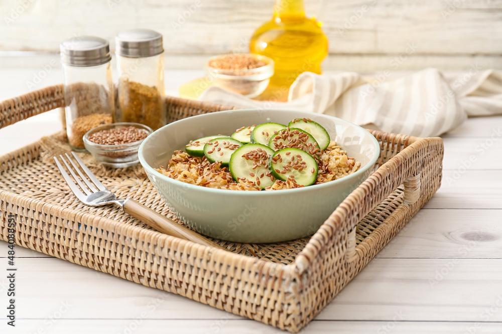 Bowl with tasty oatmeal, flax seeds and cucumber on tray