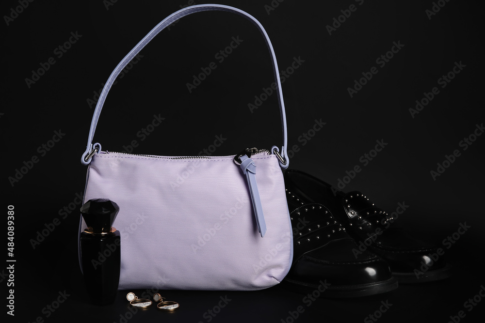 Stylish handbag, shoes, perfume and earrings on dark background