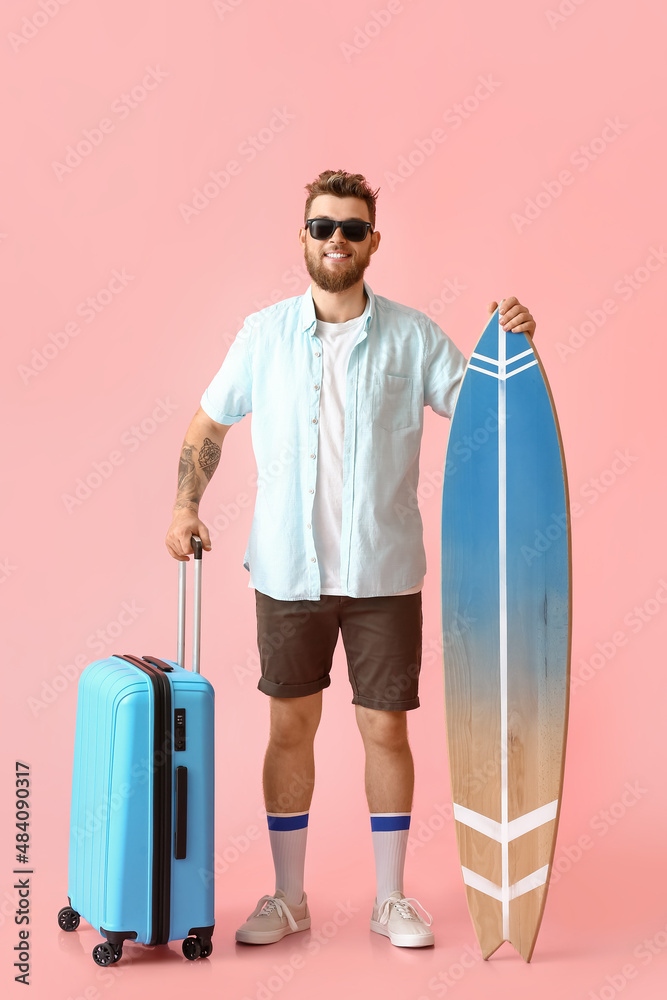 Handsome man with surfboard and suitcase on pink background