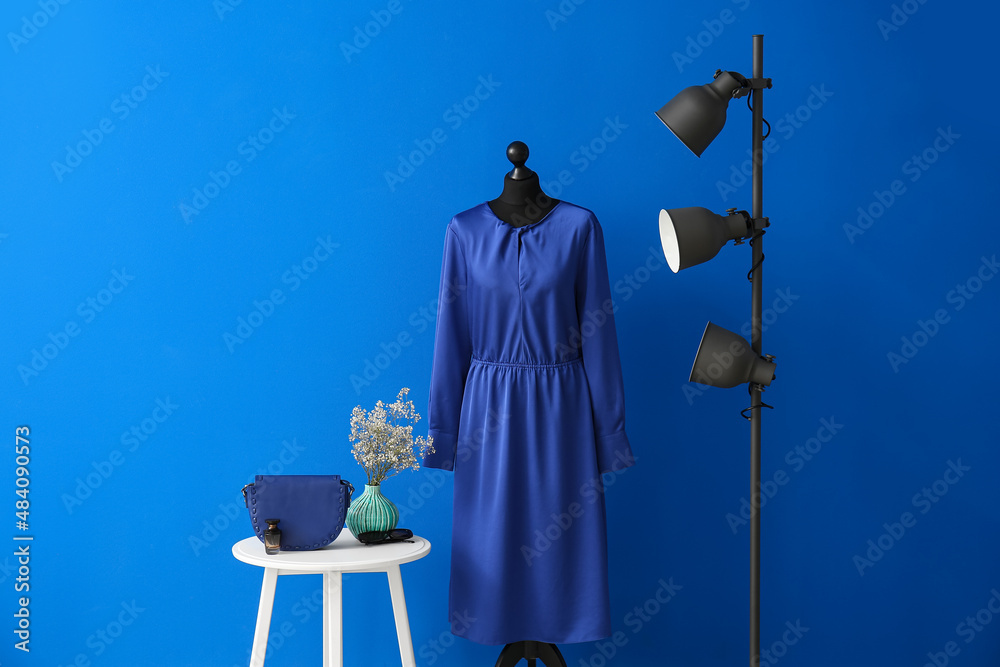 Mannequin with elegant dress, table and floor lamp near color wall