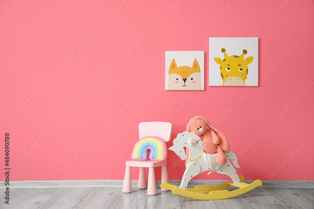 Cute rabbit sitting on rocking horse and chair with rainbow toy near color wall