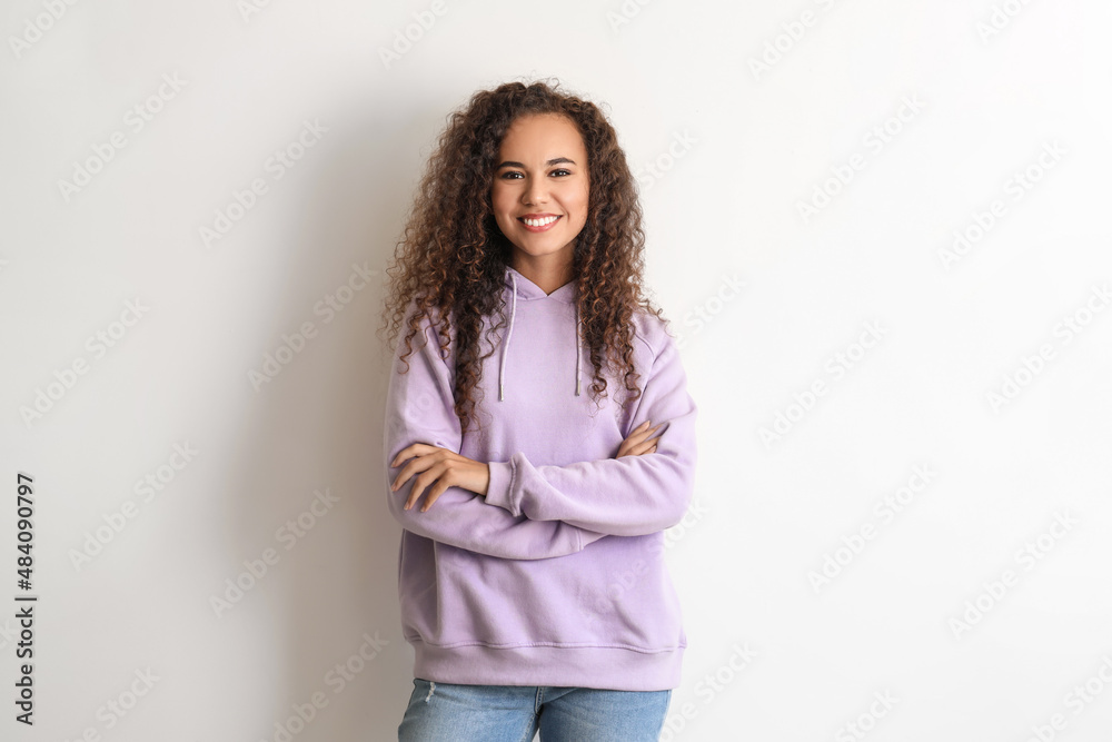 Beautiful young African-American woman in stylish hoodie on light background