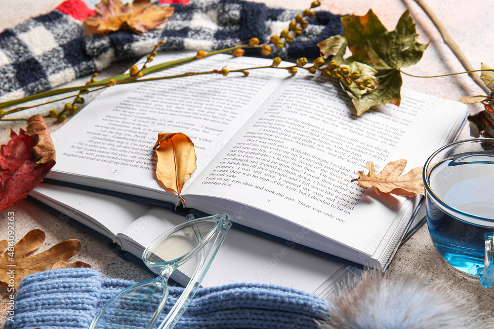 Books, cup of tea, eyeglasses and autumn decor on light background, closeup