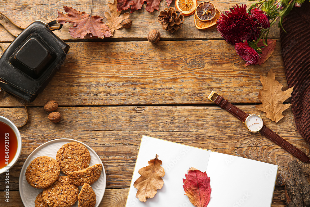 Frame made of book, cup of tea, cookies, wristwatch and autumn decor on wooden background