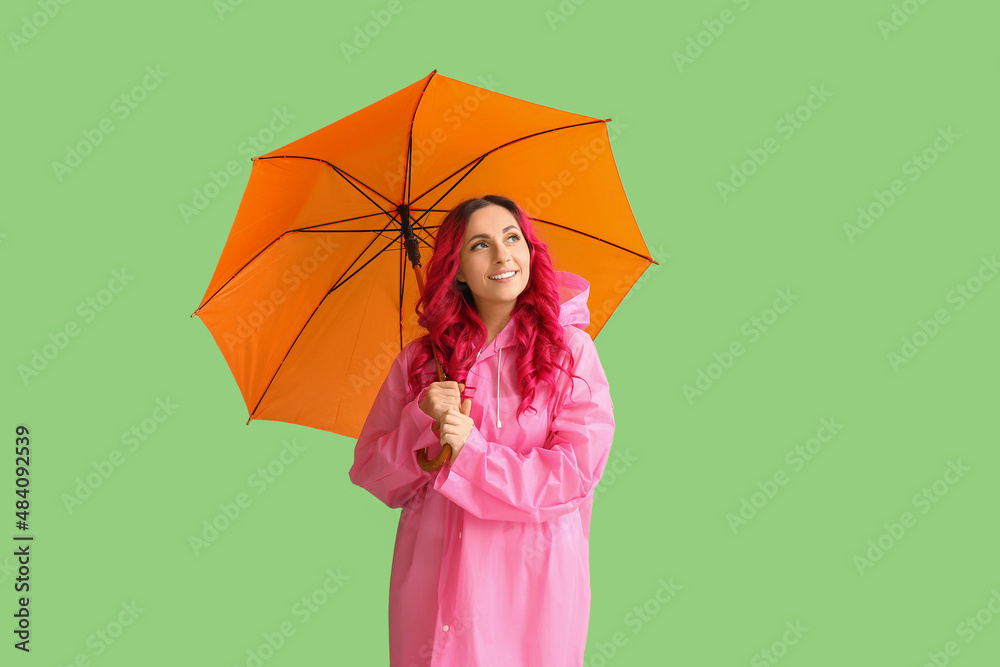 Beautiful woman in raincoat and with umbrella on color background