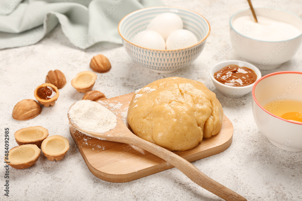 Wooden board of fresh dough for preparing walnut shaped cookies with boiled condensed milk and ingre