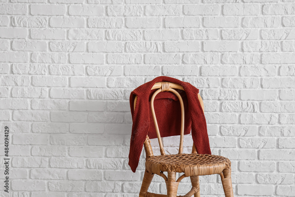 Childrens sweater on chair near white brick wall