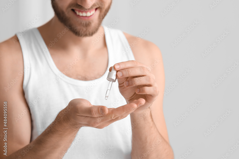 Young man using serum for skin care in bathroom