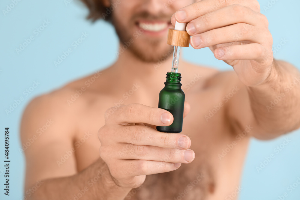 Young man with serum for skin care on color background, closeup