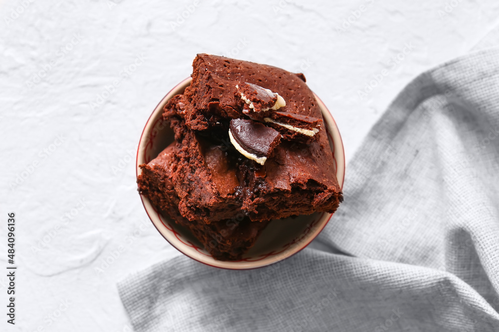 Bowl with pieces of tasty chocolate brownie on white background