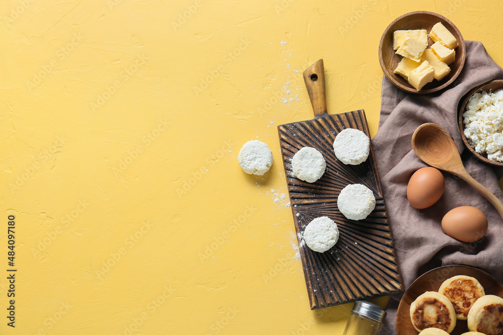 Wooden board with uncooked cottage cheese pancakes and ingredients on yellow background