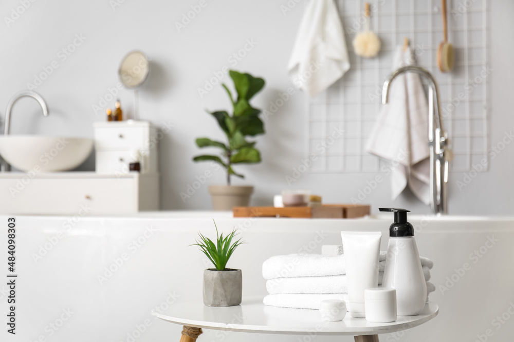 Set of cosmetic products, towels and plant on table in bathroom