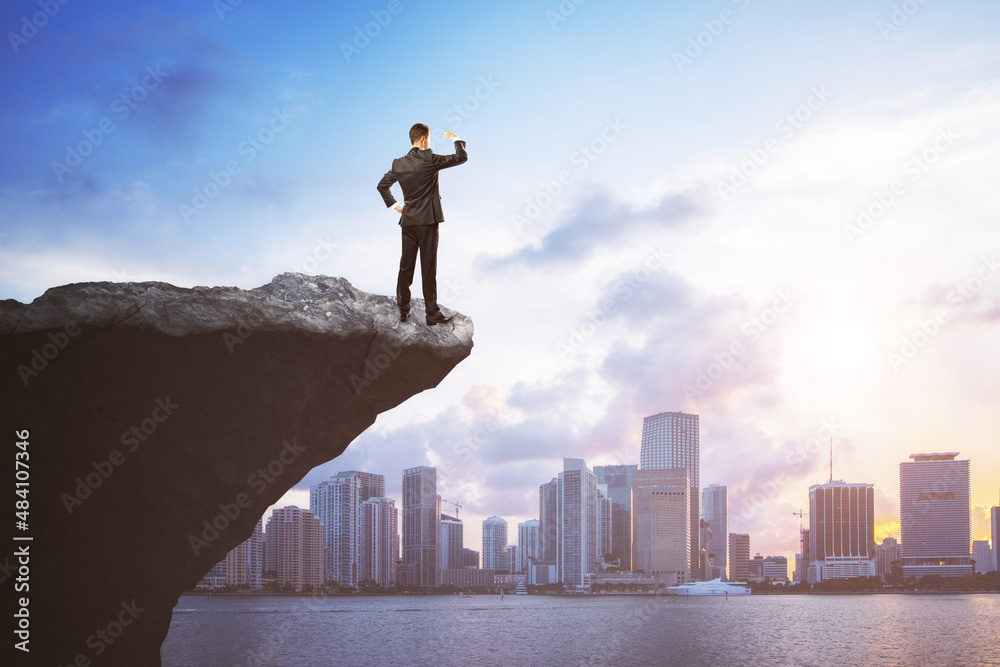 Attractive young european man on cliff edge looking into the distance on bright city background with