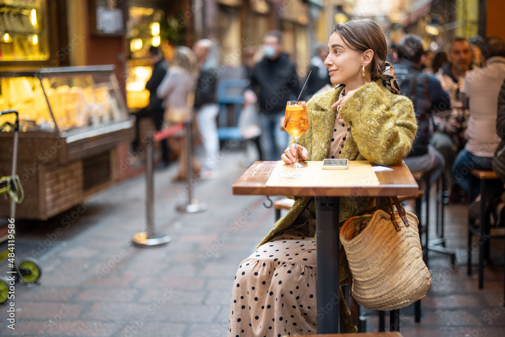 Woman sitting with a cocktail at outdoor bar or restaurant on the crowded street in Bologna. Concept