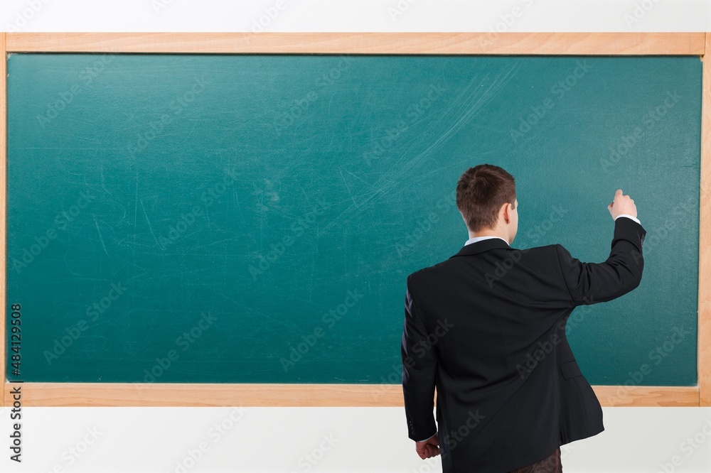 Student child writes with chalk on a blackboard solution of an example in mathematics.