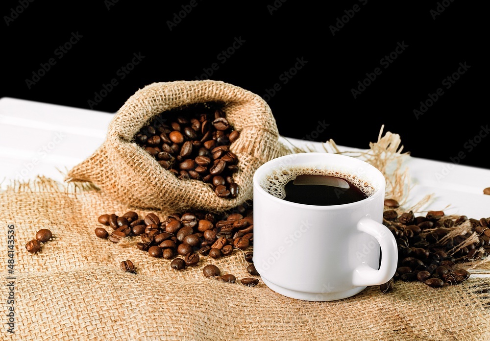 Hot coffee in a white coffee cup and many beans placed around