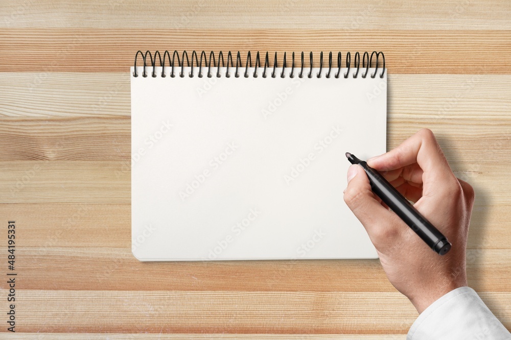 Females hand writing in white blank open notebook with pen