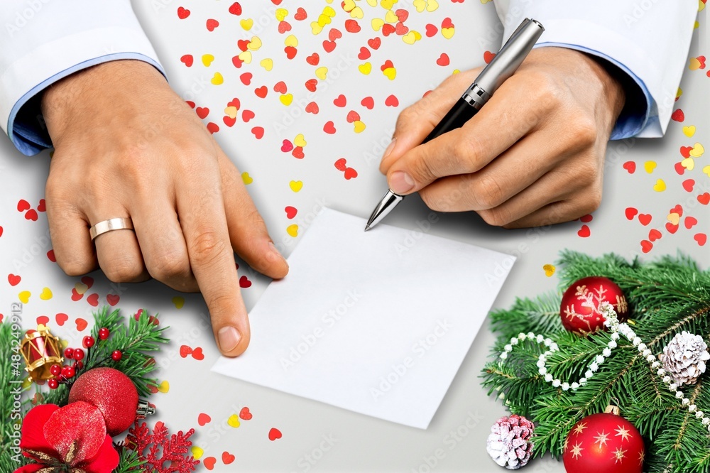 Human writing in notebook at table with Christmas decor,. New Year aims