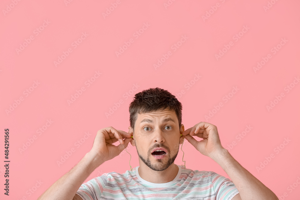 Shocked handsome man with ear plugs on pink background