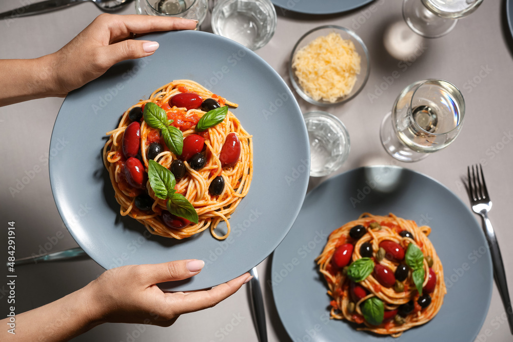 餐厅服务员在餐桌上端着一盘美味的Pasta Puttanesca