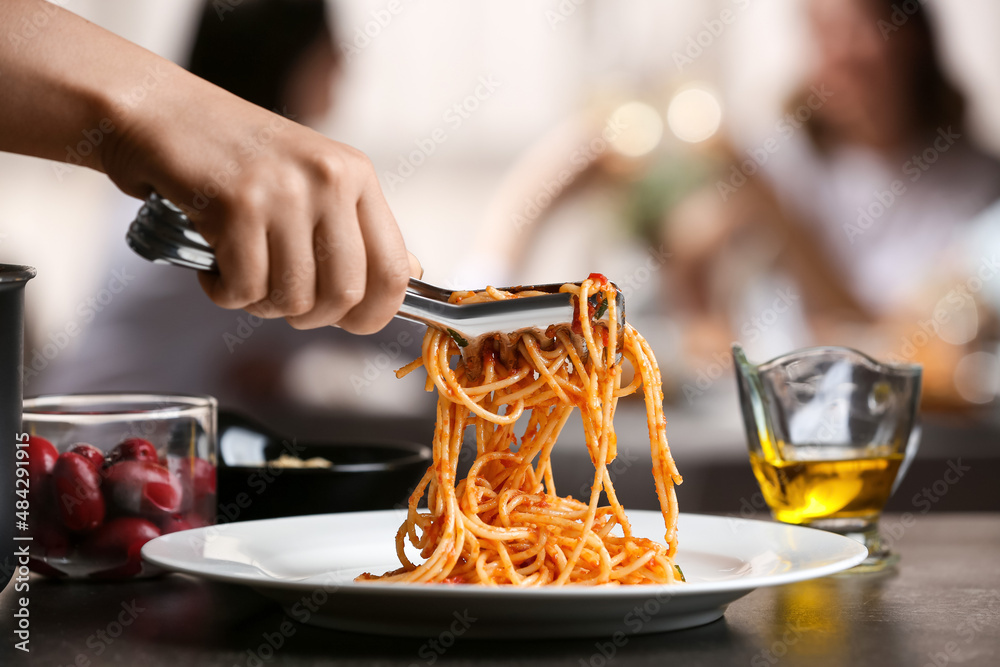 Woman putting tasty Pasta Puttanesca on plate at table in restaurant