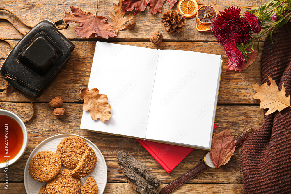 Book, cup of tea, cookies and autumn decor on wooden background