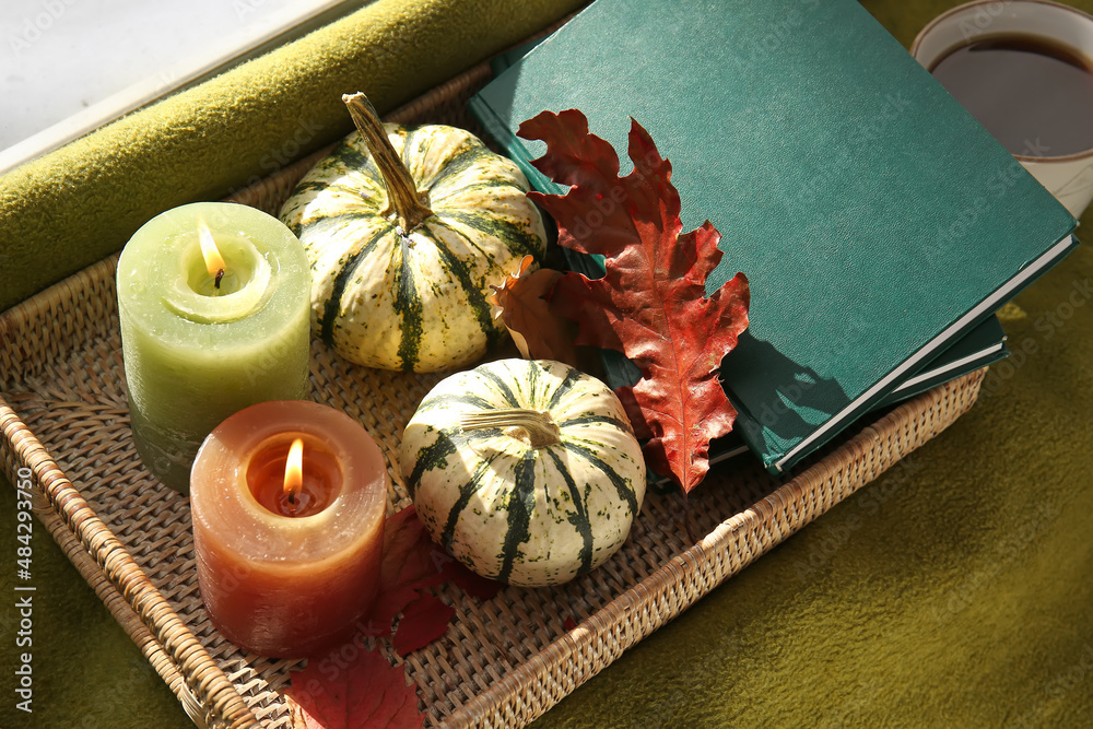 Tray with books, pumpkins and candles on plaid in room