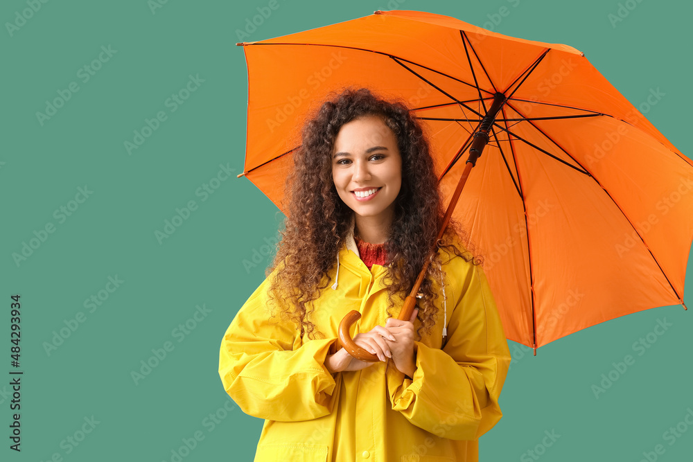 身穿黄色雨衣、绿色背景带伞的年轻非裔美国妇女