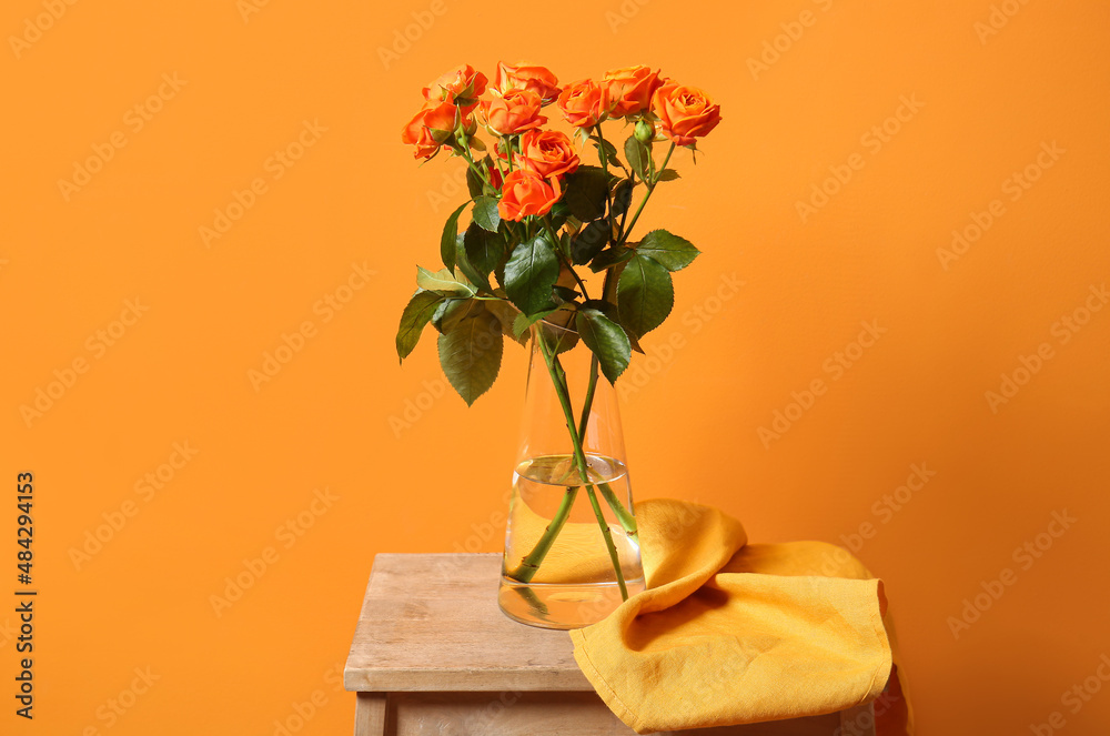 Vase with beautiful orange roses on table against color wall