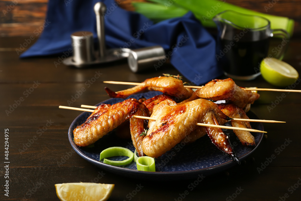 Plate with grilled chicken wings skewers on dark wooden background