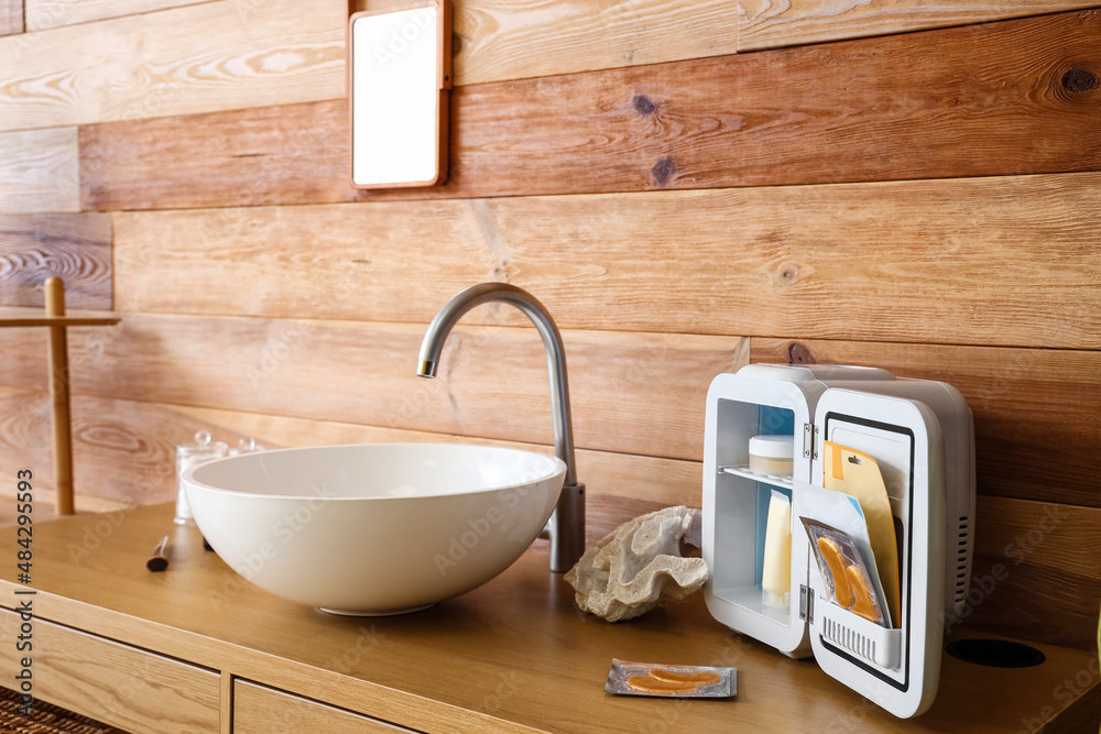 Open cosmetic refrigerator and sink on table near wooden wall