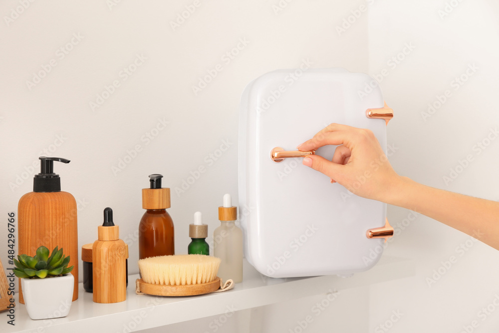 Female hand with small refrigerator and cosmetic products on shelf