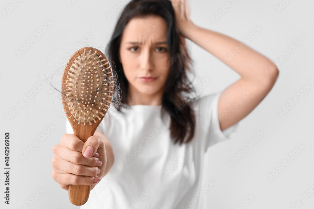 Young woman with hair loss problem on light background